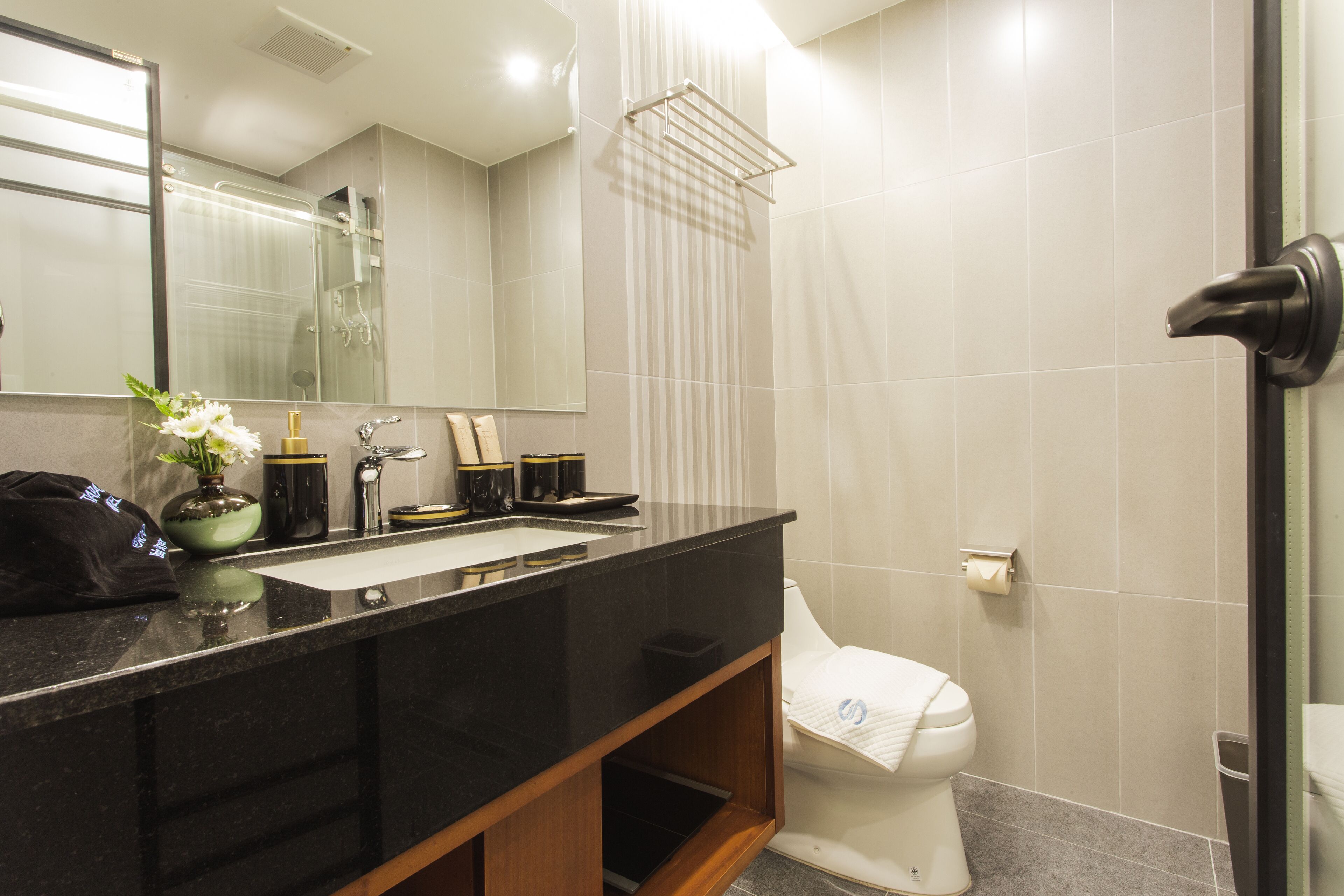 A modern bathroom with a black countertop, a white toilet, a shower with a glass door, and a mirror above the sink.
