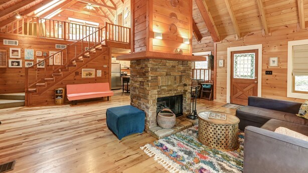 A spacious log cabin interior with a stone fireplace, wooden staircase, and a cozy seating area. - Respite at Big Canoe - Wood-burning fireplace, bright interiors, Wifi (Jasper)