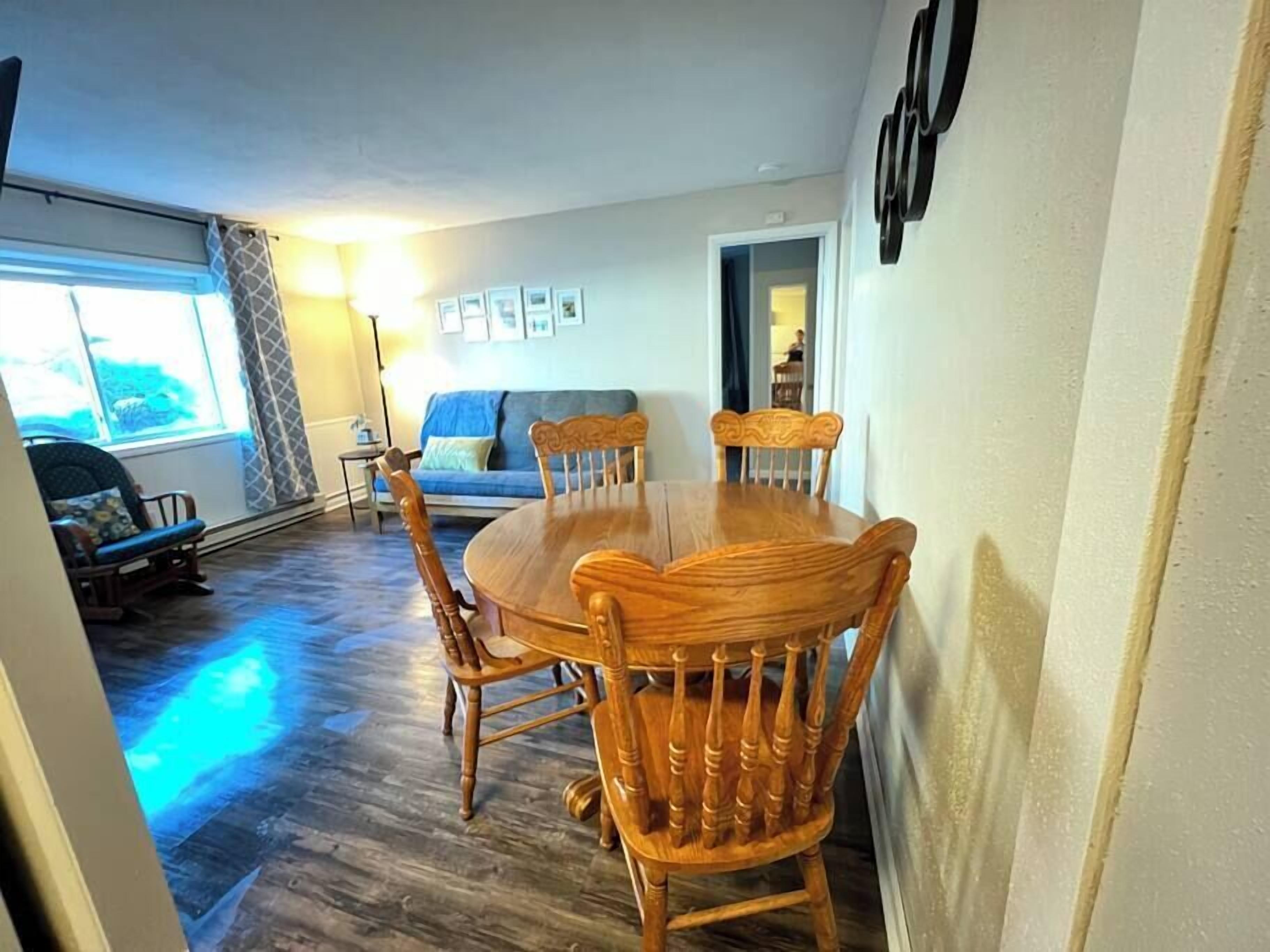 A dining area with a wooden table and chairs, a sofa, and a window with curtains.