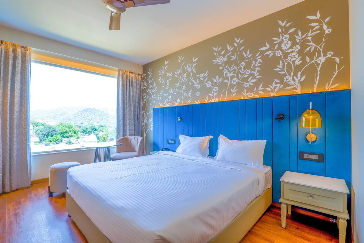 Habitación de hotel con una cama grande, una mesita de noche, una silla y una ventana con cortinas.
