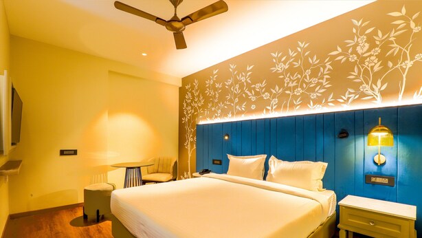 A hotel room with a large bed, a ceiling fan, a wall-mounted lamp, and a small table with a chair. - 7 Apple Hotel Jal Mahal Jaipur (Jaipur)
