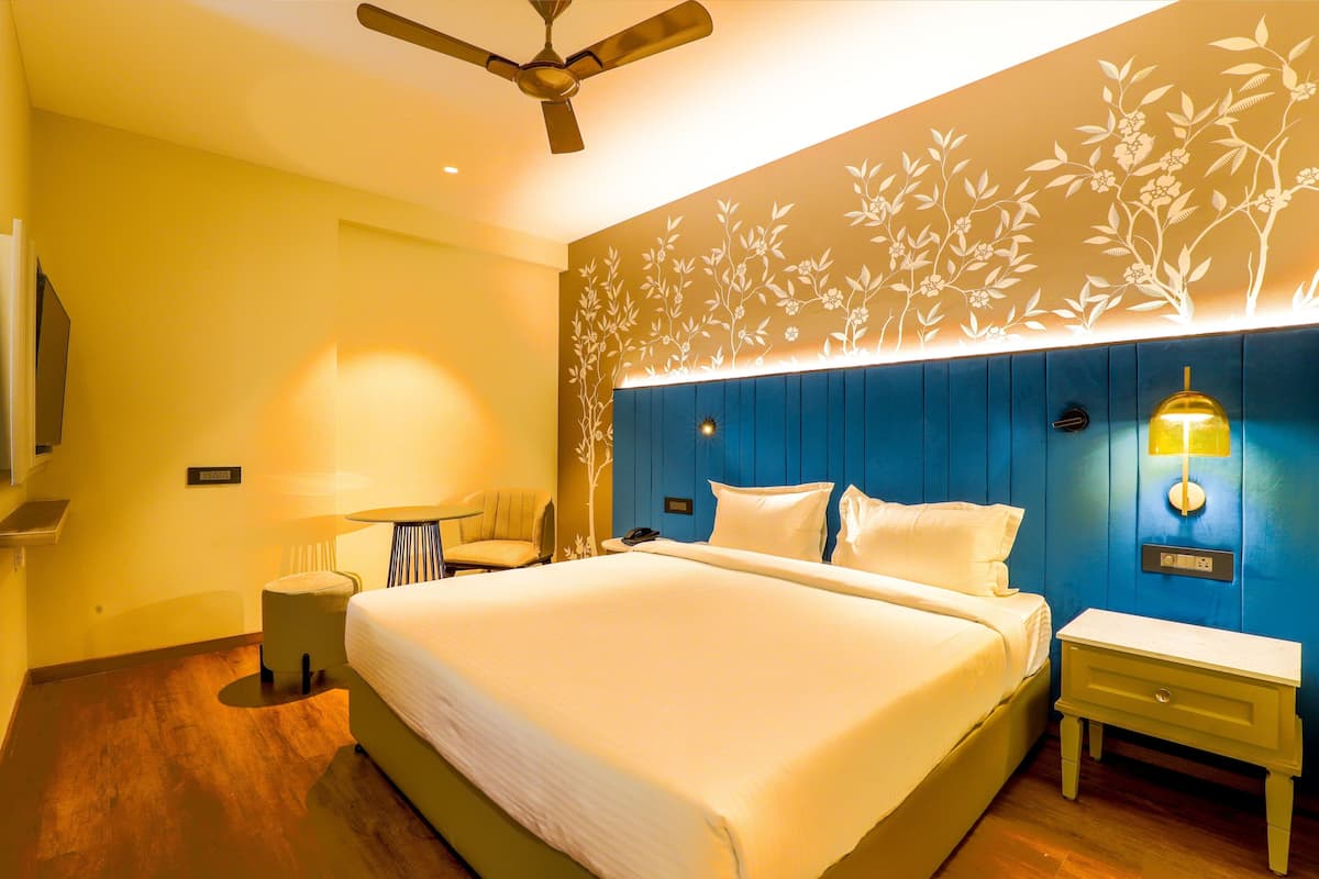Una habitación de hotel con una cama grande, un ventilador de techo, una lámpara de pared y una pequeña mesa con una silla.