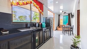 A modern kitchen with a black countertop, a sink, and a window with a red curtain. There is a water dispenser and a refrigerator in the background. - Villas Mapache del Caribe (Cahuita)