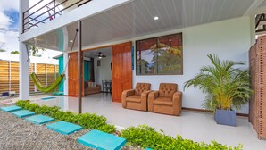 A modern house with a patio area featuring a hammock, two sofas, and a potted plant. - Villas Mapache del Caribe (Cahuita)