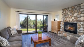 Una sala de estar con chimenea de piedra, un sofá, una mesa de centro y vistas al exterior a través de amplios ventanales.