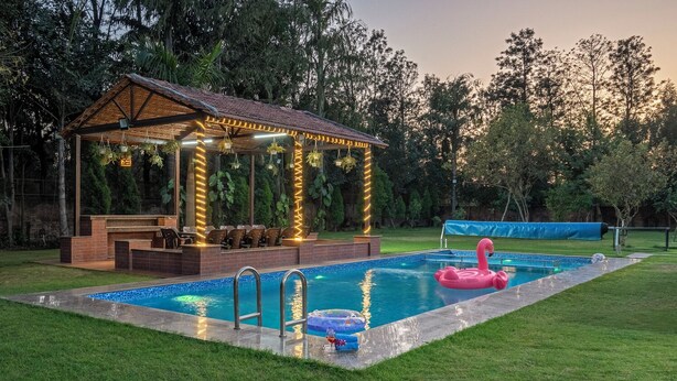 A pool with a lounge area, a covered seating area, and a flamingo float. - The Orchard Farm, Manesar- Luxury Pet- Friendly Farm with private pool & Jacuzzi (Para)