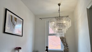 A staircase with a wooden handrail, a chandelier, a framed picture on the wall, and a window with a view of a brick building. - Brecon View by Switchback Stays (Newport)