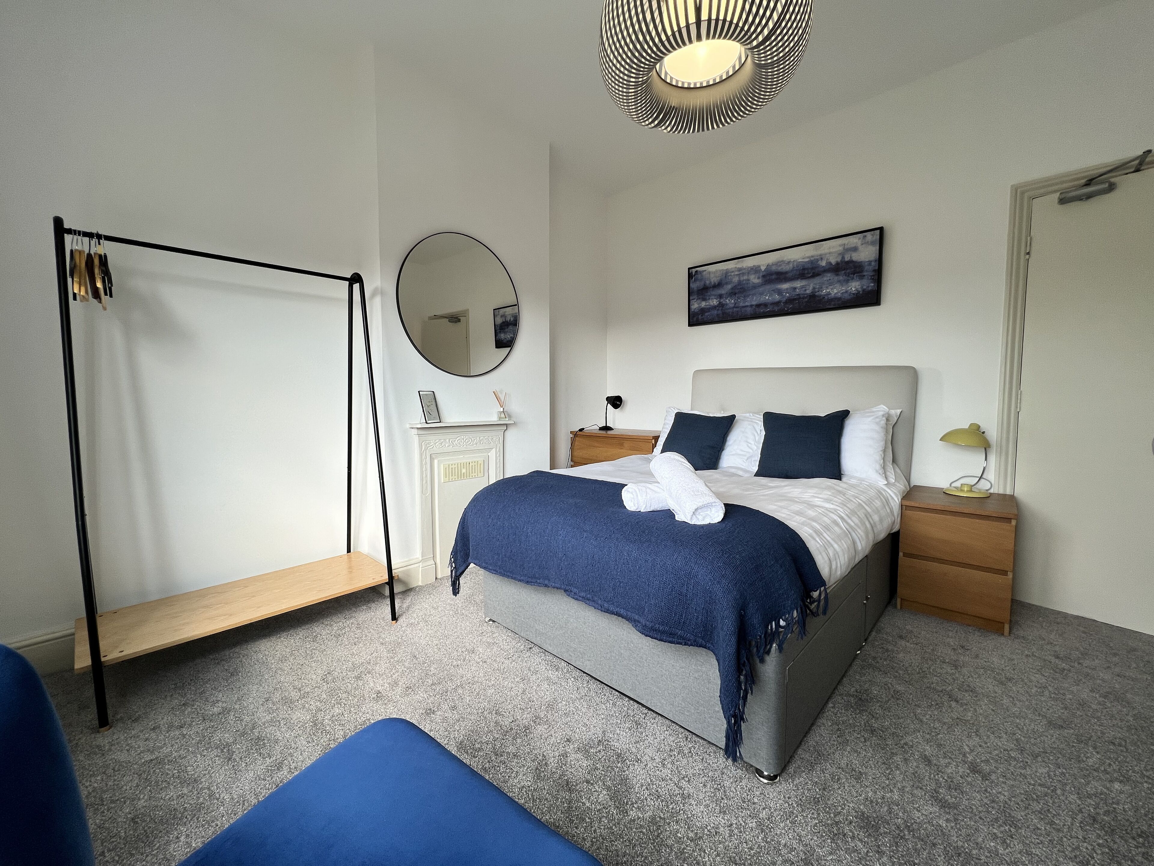 A modern bedroom with a bed, bedside tables, a mirror, and a hanging light fixture.