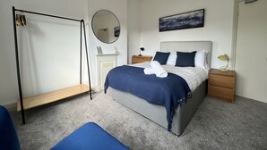 A modern bedroom with a bed, bedside tables, a mirror, and a hanging light fixture. - Brecon View by Switchback Stays (Newport)