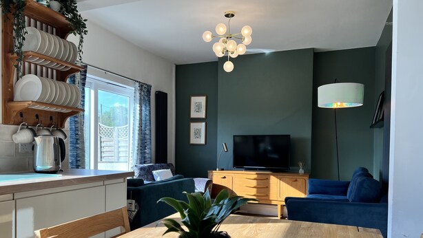 A modern living room with a wooden dining table, a blue sofa, a TV, and a chandelier. - Brecon View by Switchback Stays (Newport)