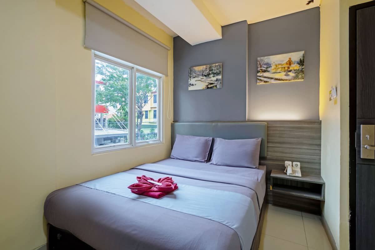 A hotel room with a bed, a window, a painting, and a telephone on a nightstand.