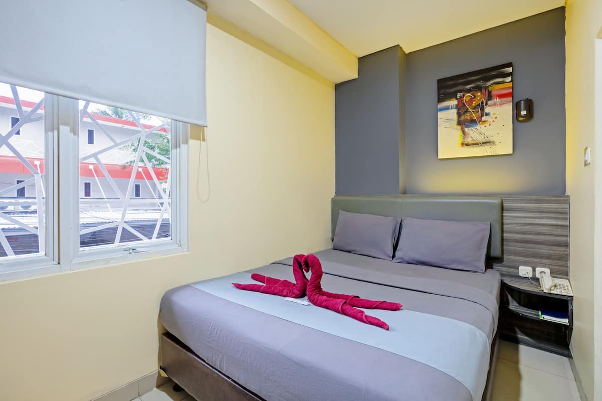 A hotel room with a bed, a window, a painting on the wall, and a telephone on the nightstand.