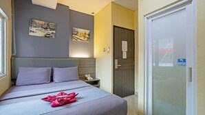 A hotel room with a bed, two pillows, a bedside table with a phone, and two paintings on the wall. - City Biz Residence (Jakarta)