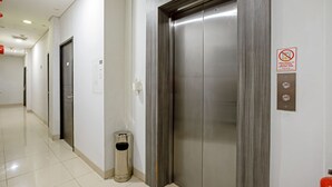 A clean, modern hallway with an elevator, a trash can, and a no-smoking sign. - City Biz Residence (Jakarta)
