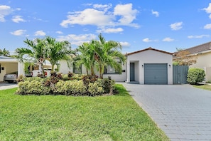 A modern two-story house with a paved driveway, a garage, and a well-maintained lawn with palm trees.