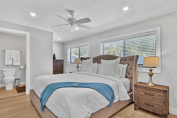 A bedroom with a bed, a nightstand, a dresser, a ceiling fan, and a window with blinds.