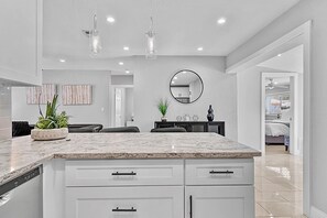 A modern kitchen with white cabinetry, a marble countertop, and pendant lighting. - The Perfect Get Away - Walk to Wilton Drive (Wilton Manors)