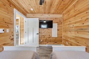 A wooden cabin room with a bed, a TV, and a door leading to another room. - Treeside Retreat with Hot tub (Windsor)