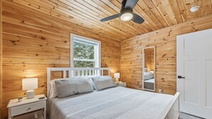 A wooden-paneled bedroom with a bed, nightstands, a ceiling fan, and a window. - Treeside Retreat with Hot tub (Windsor)