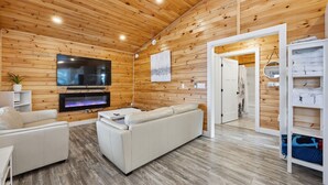 A cozy living room with a flat-screen TV, a fireplace, and a white sofa. - Treeside Retreat with Hot tub (Windsor)