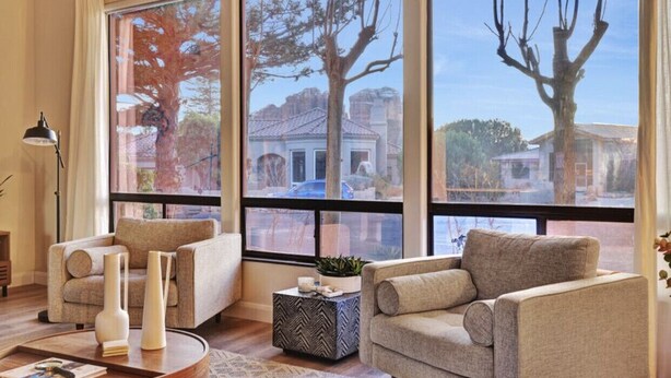 A living room with two sofas, a coffee table, and a side table. Large windows provide a view of the outside.
