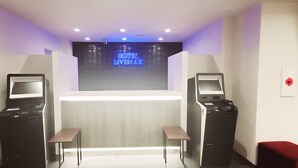 A hotel reception area with a digital display, two self-service kiosks, and a small table. - Hotel Livemax Kamata Ekimae (Tokyo)