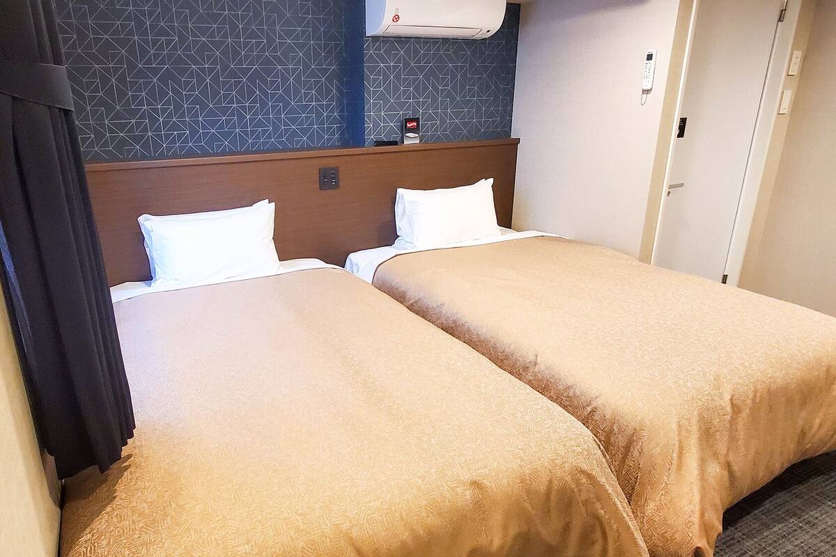 A hotel room with two beds, a headboard, a telephone, and a wall-mounted air conditioner.