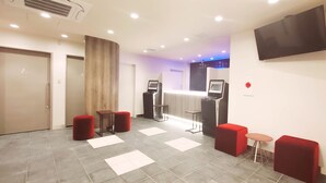 A hotel lobby with a reception desk, self-service kiosks, red seating, and a TV mounted on the wall. - Hotel Livemax Kamata Ekimae (Tokyo)