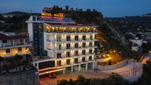 Un hotel de varios pisos con un letrero llamativo en la azotea, varios balcones y una entrada bien iluminada.