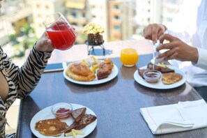 Un desayuno con tortitas, tostadas y una bandeja de fruta sobre una mesa.