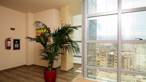 Habitación amplia con un gran ventanal que ofrece vistas a la ciudad, una planta en maceta, un extintor y un cartel que indica el nivel del piso.