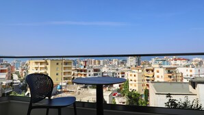 Un balcón con una mesa redonda y una silla negra, con vistas a un paisaje urbano con varios edificios.