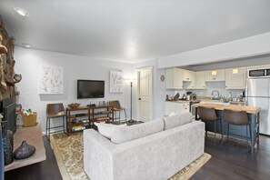 A modern living room with a sofa, a TV, and a dining area with chairs and a table.