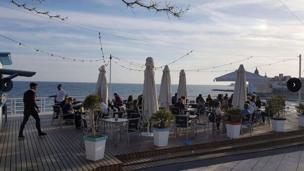 Een terras met tafels en parasols, met uitzicht op de zee.
