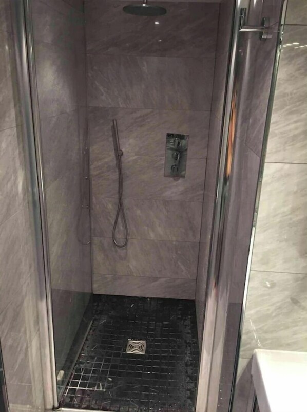 Une cabine de douche fermée par des parois en verre, dotée d’un sol carrelé et d’un pommeau de douche.