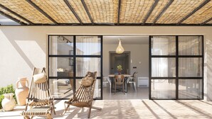 Un espacio habitable de concepto abierto con una puerta de vidrio que da a un comedor, mobiliario exterior con sillas y una mesa, y un techo con un diseño tejido.