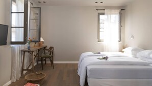 Un dormitorio con cama, escritorio y silla, ventana con cortinas y televisor en la pared.