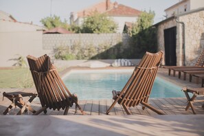 Two wooden lounge chairs by a swimming pool with a stone wall and a building in the background. - Stunning 4-bed House in Zadar (Zadar)