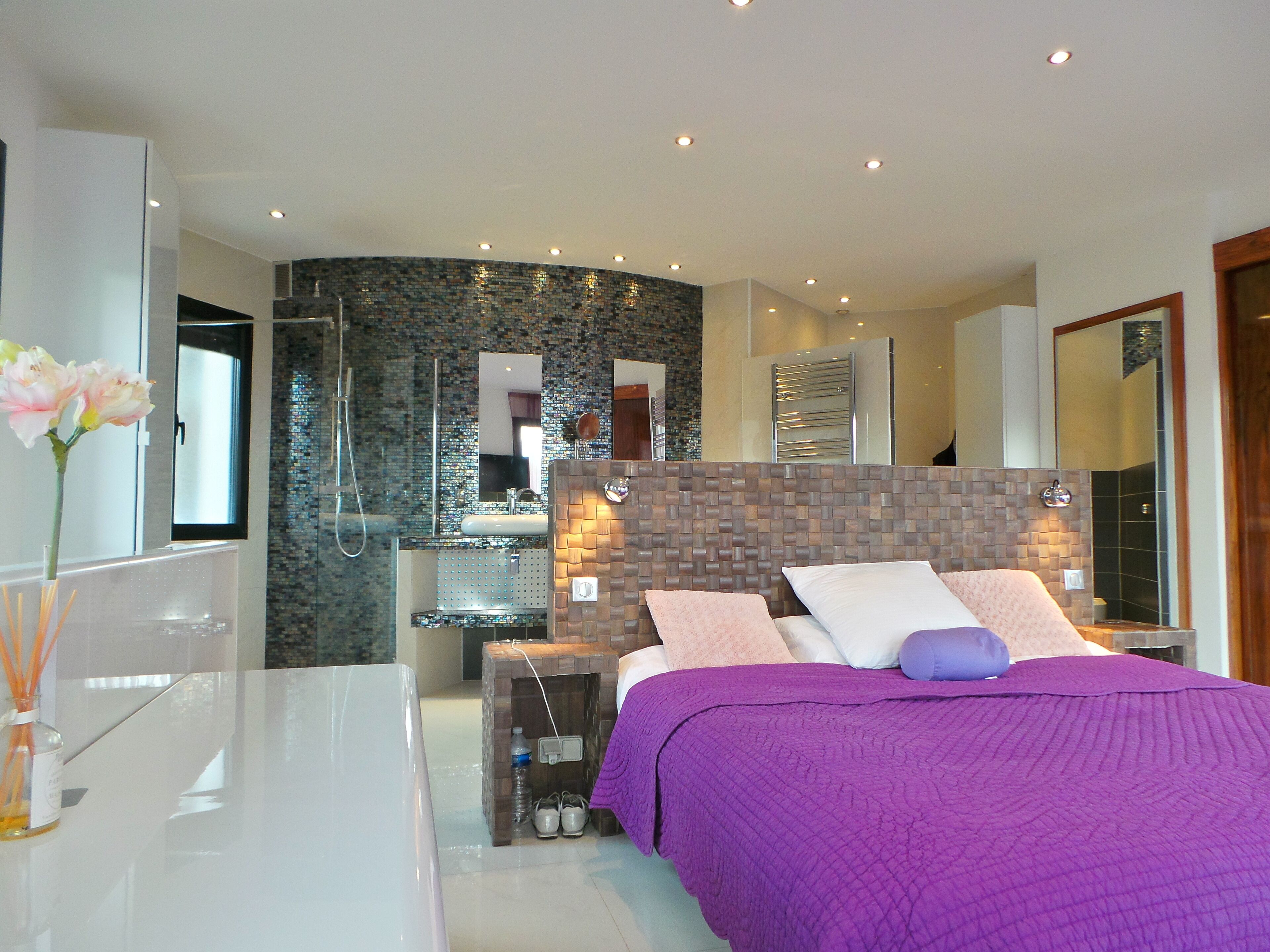 Une chambre à coucher moderne avec un grand lit, une salle de bain dotée d’une douche en verre et une coiffeuse blanche.