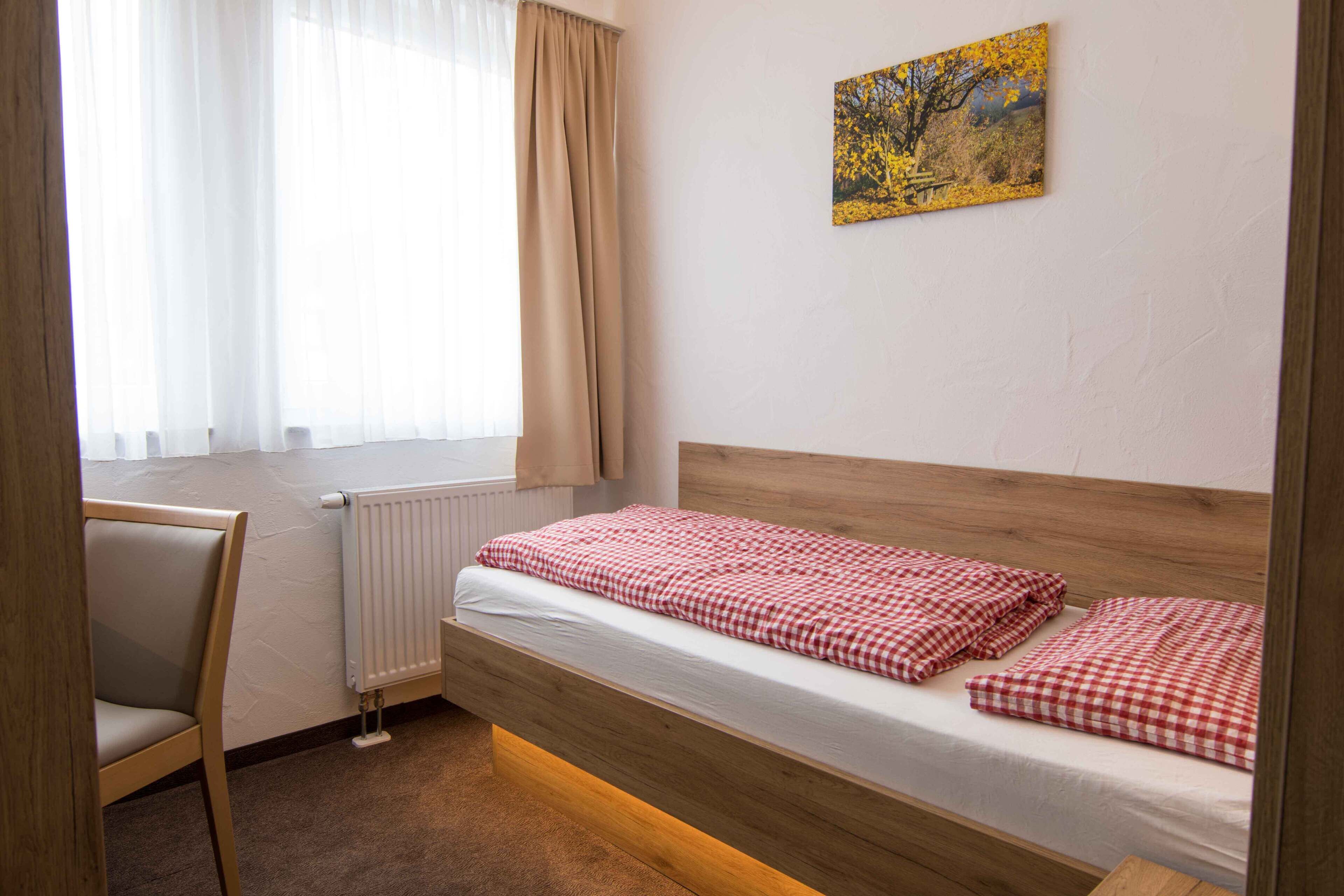 Una camera da letto con un letto di legno, una sedia, un termosifone e una finestra con tende.