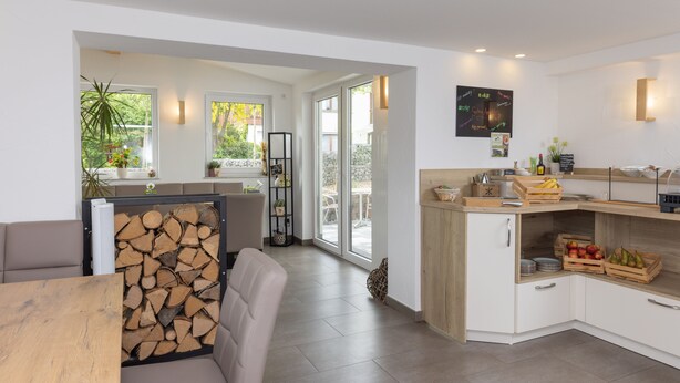 A modern kitchen with a dining area, large windows, and a built-in wood storage unit. - Pension Klein (Bad Laasphe)
