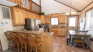 A spacious kitchen with wooden cabinets, a large island with bar stools, a dining table with chairs, and a chandelier. - Oceanside, Private Pool, Hot Tub, MIL Suite, KH529, Sea Turtle Sunrise (Kitty Hawk)
