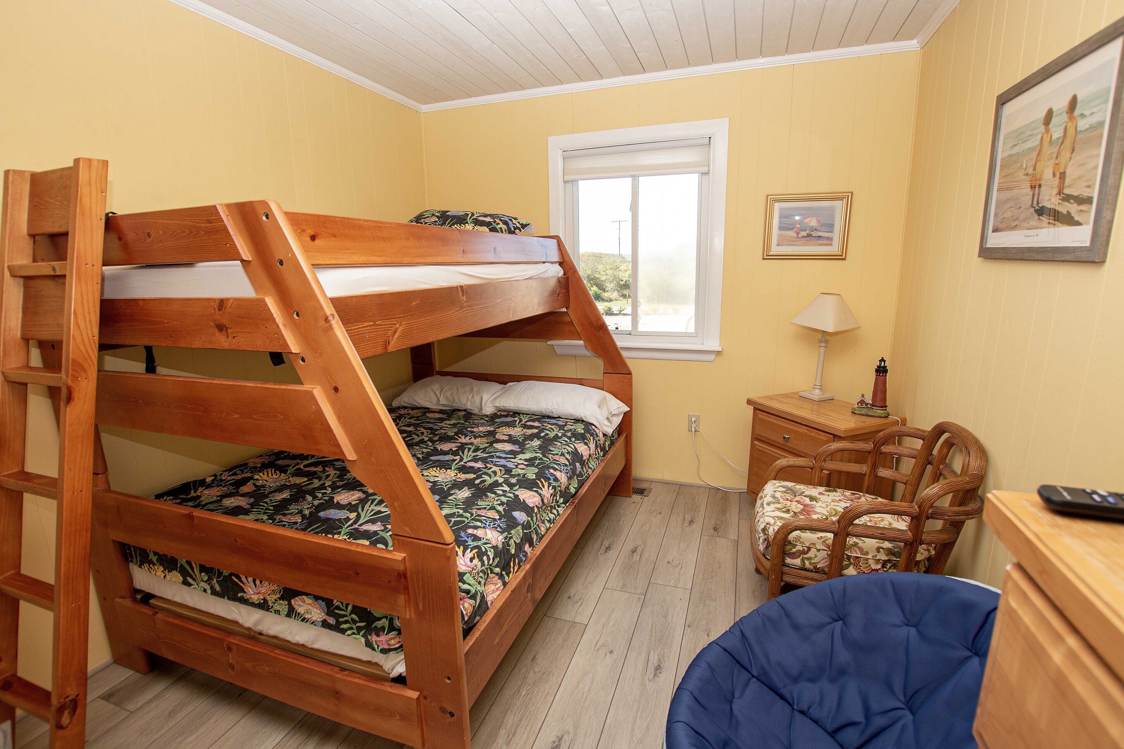 A bunk bed with a ladder, a desk with a lamp, and a chair in a room with yellow walls and a window.