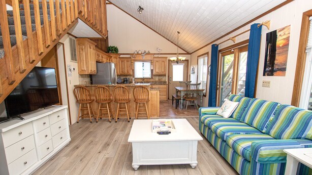 A spacious living area with a wooden staircase, a kitchen with wooden cabinets, a dining area with a striped sofa, and a white coffee table. - Oceanside, Private Pool, Hot Tub, MIL Suite, KH529, Sea Turtle Sunrise (Kitty Hawk)