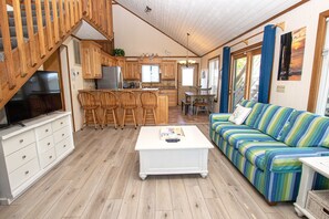 A spacious living area with a wooden staircase, a kitchen with wooden cabinets, a dining area with a striped sofa, and a white coffee table. - Oceanside, Private Pool, Hot Tub, MIL Suite, KH529, Sea Turtle Sunrise (Kitty Hawk)