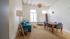 A room with a teal sofa, a wooden dining table with chairs, a floor lamp, and a large window. - Pretty town house in the heart of Chinon + garden 6 p. (Chinon)