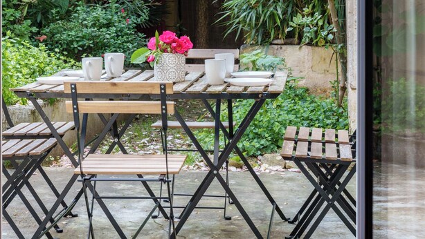 An outdoor patio with a wooden table and chairs, surrounded by lush greenery and flowering plants. - Pretty town house in the heart of Chinon + garden 6 p. (Chinon)
