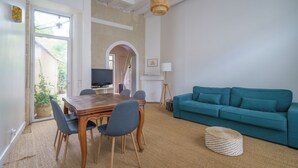 A living room with a teal sofa, a wooden dining table with chairs, a woven pouf, and a TV in the background. - Pretty town house in the heart of Chinon + garden 6 p. (Chinon)