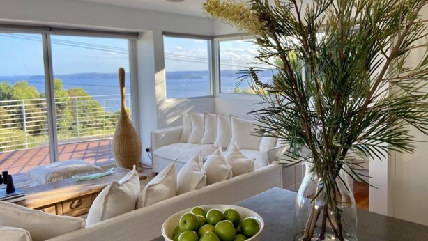A modern living room with a white sofa, a coffee table with a bowl of green apples, and a tall vase with a plant.