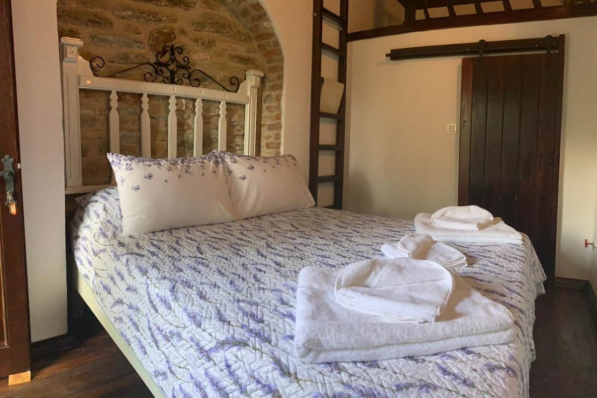 A bedroom with a stone archway, a wooden ladder, a bed with a floral-patterned duvet, and a set of towels on the bed.